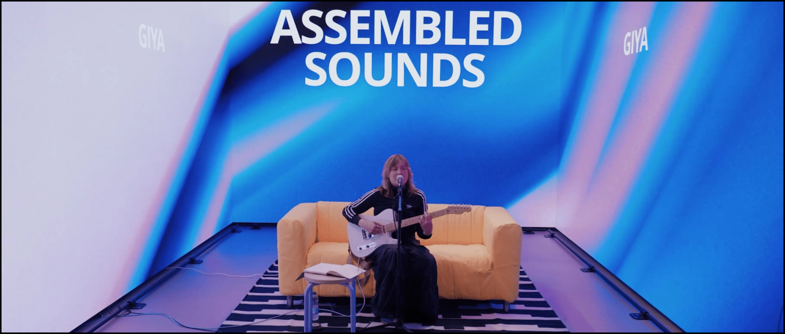 IKEA immersive studio hero image. A woman playing a guitar on a sofa amongst the immersive LED screens. The music show is live streamed to online audiences