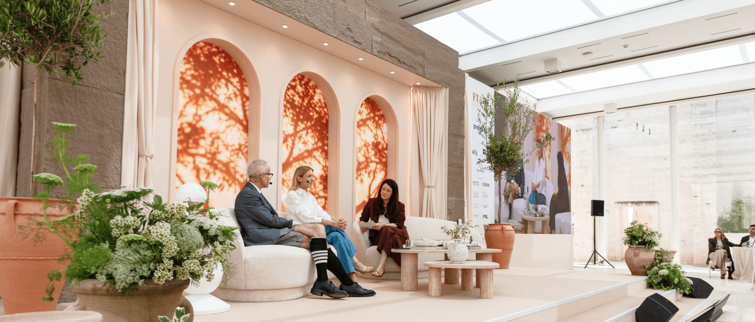 scenic stage build featuring custom arched backdrop panels and plants. the speaker panel are on stage with props and soft furnishings